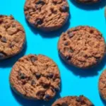 1Round cookies with chocolate chips are placed in a pattern on a bright blue surface. The cookies have a golden brown color and a chewy texture.